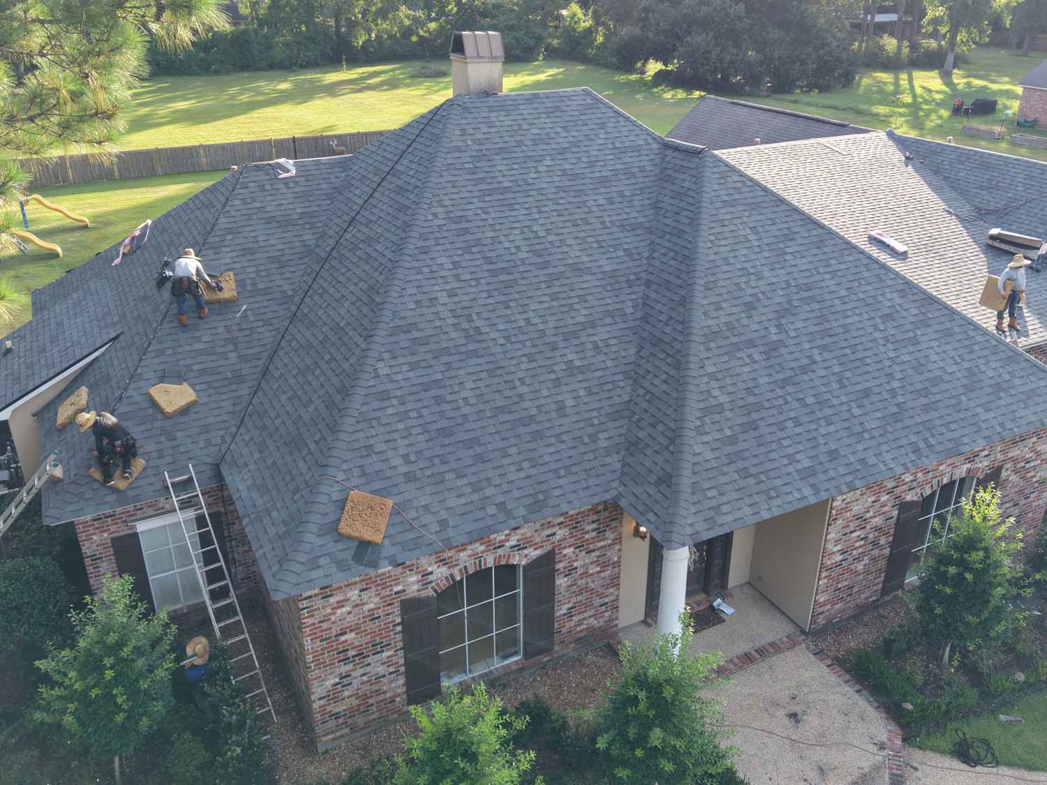 Aerial drone view of an Exterior Pros crew installing a new roof on a brick home in Ascension Parish, Louisiana